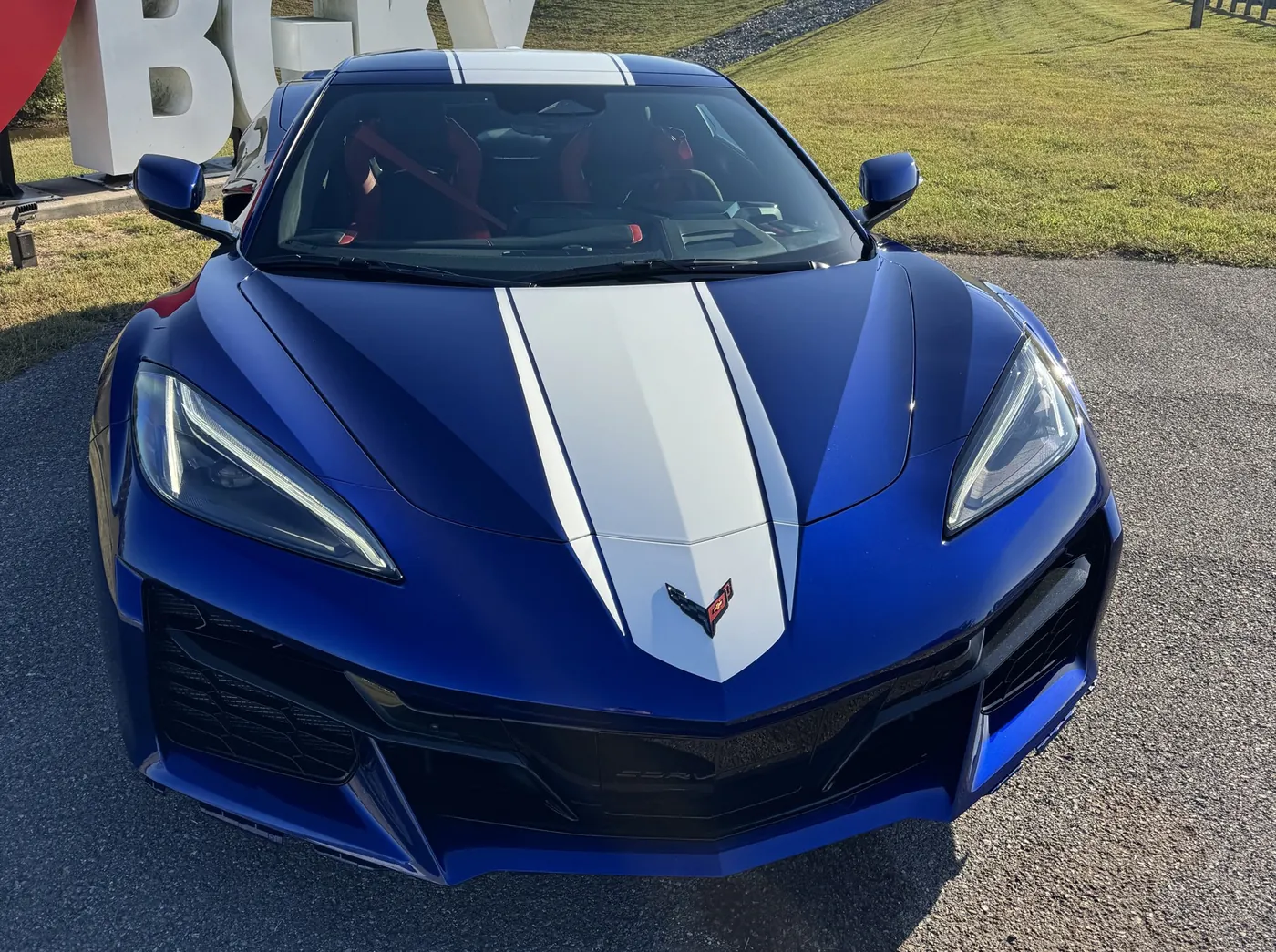 The front of a blue Corvette with a white stripe leading to the crossed flags badge